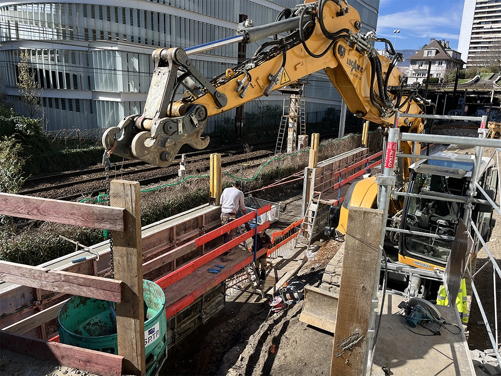 un ouvrier et une pelleteuse sur un chantier pour la création d'un mur de soutènement en bord de voie ferrée en centre ville de Chambéry